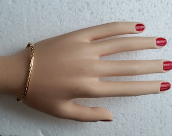 May include: A gold bangle bracelet with a textured design. The bracelet is on a mannequin hand with red nail polish.