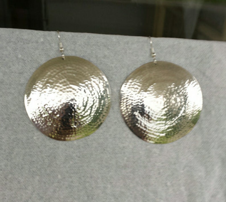 May include: A pair of silver oval-shaped earrings with a hammered texture.