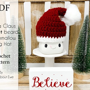 May include: Crochet pattern for a Santa Claus mug hat without a beard. The hat is red with a white pom-pom and white trim. The mug is white with a smiling face. The pattern is by Knots About Ewe.