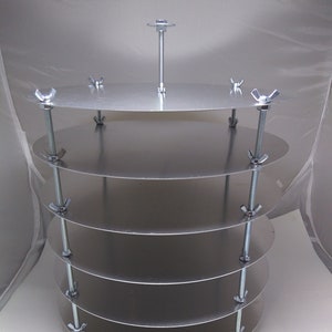 May include: A silver metal cake stand with five tiers and a central support rod. Each tier is held in place by three wing nuts and bolts. The stand has red plastic feet.