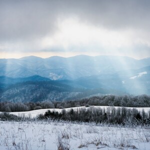 May include: A snowy mountain landscape with a cloudy sky and sunbeams shining through the clouds.