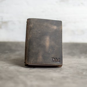 May include: A brown leather journal with the initials "DM" embossed on the front cover.