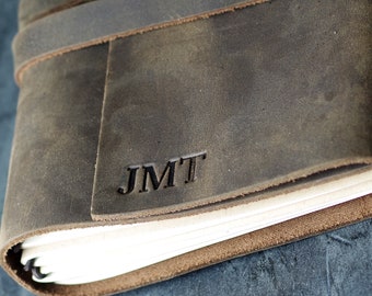 May include: A brown leather journal with a personalised inscription "JMT" on the front cover.