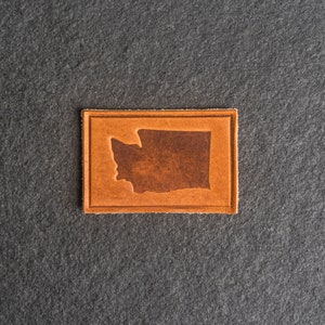 May include: A brown leather patch with a silhouette of the state of Washington in a darker brown colour.