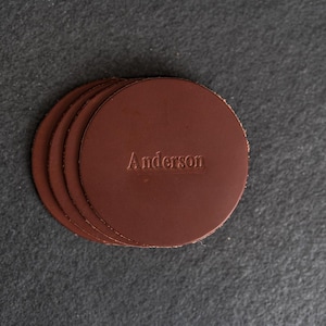 May include: Set of four brown leather coasters with the name "Anderson" embossed on the top.