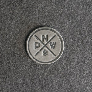May include: A grey leather patch with a compass rose design and the letters "N", "P", "W" inside a circle. A small pine tree is in the centre of the compass rose.