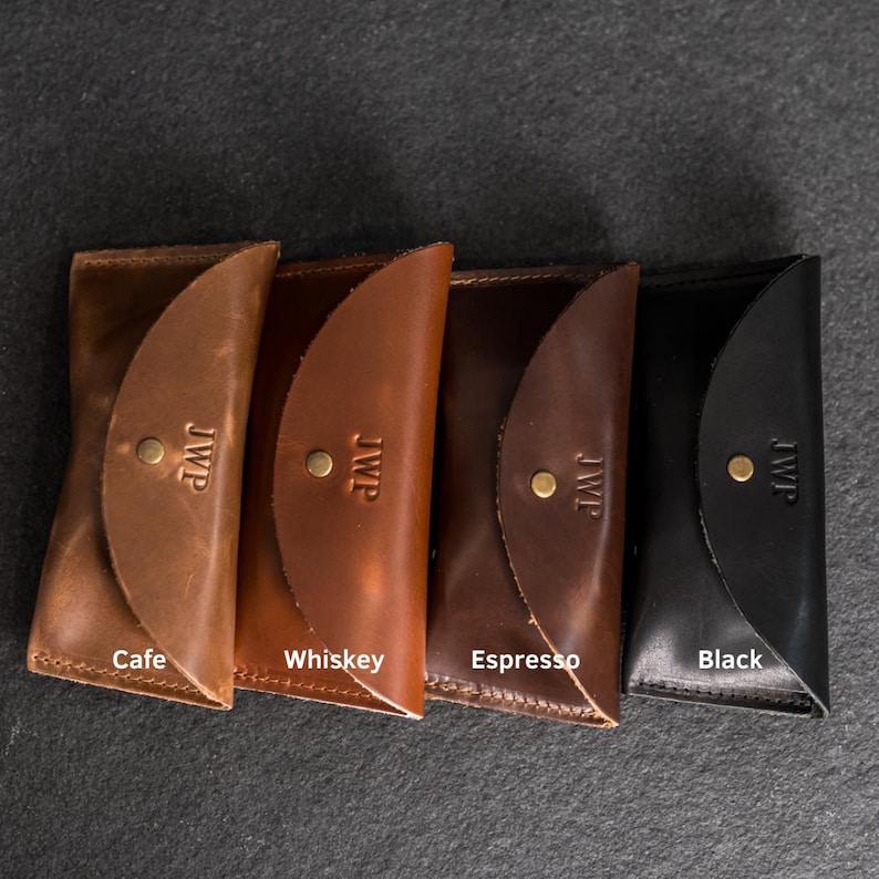 Puede incluir: Cuatro carteras de cuero en tonos marr&oacute;n y negro, cada una con cierre de solapa y bot&oacute;n de lat&oacute;n. Las carteras est&aacute;n etiquetadas como "Cafe", "Whiskey", "Espresso" y "Black". Cada cartera est&aacute; grabada con las iniciales "JWP".