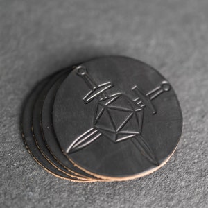 Puede incluir: Juego de cuatro posavasos de cuero negro con un diseño de dos espadas cruzadas sobre un dado de veinte caras.