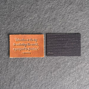 May include: A brown leather patch with the quote "Education is the key to unlocking the world, a passport to freedom."  The quote is attributed to "- Oprah Winfrey". The patch has a black adhesive backing.