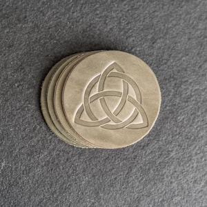 May include: A set of four brown leather coasters with a Celtic knot design.