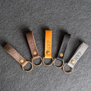 May include: Five leather keychains with metal rings. Each keychain is a different color: brown, orange, black, gray, and white. The keychains are all engraved with the letters "MWP".