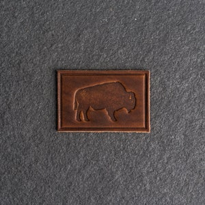 May include: A brown leather patch with a silhouette of a bison embossed in the center.