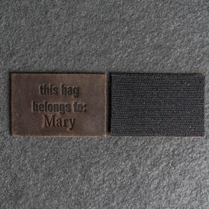 May include: Brown leather luggage tag with the text "this bag belongs to: Mary" and a black hook and loop fastener.