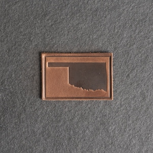 May include: A brown leather patch with the outline of the state of Oklahoma embossed in a darker brown color.