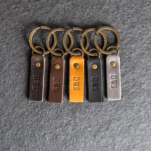 May include: Six leather keychains with brass key rings. Each keychain has the initials "DWS" embossed on the leather. The keychains are in different colors: brown, dark brown, yellow, black, gray, and light brown.