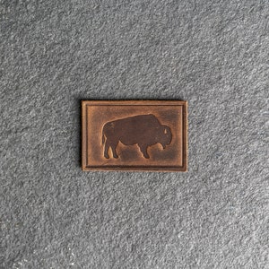 May include: A brown leather patch with a silhouette of a bison in the center.