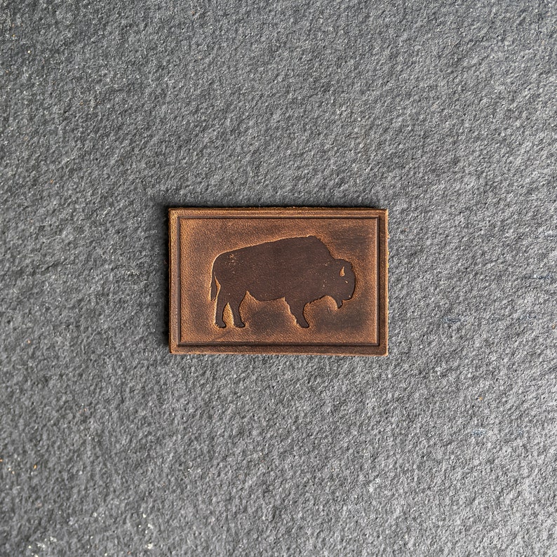 May include: A brown leather patch with a silhouette of a bison in the center.