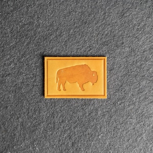 May include: A brown leather patch with a silhouette of a bison in the center.