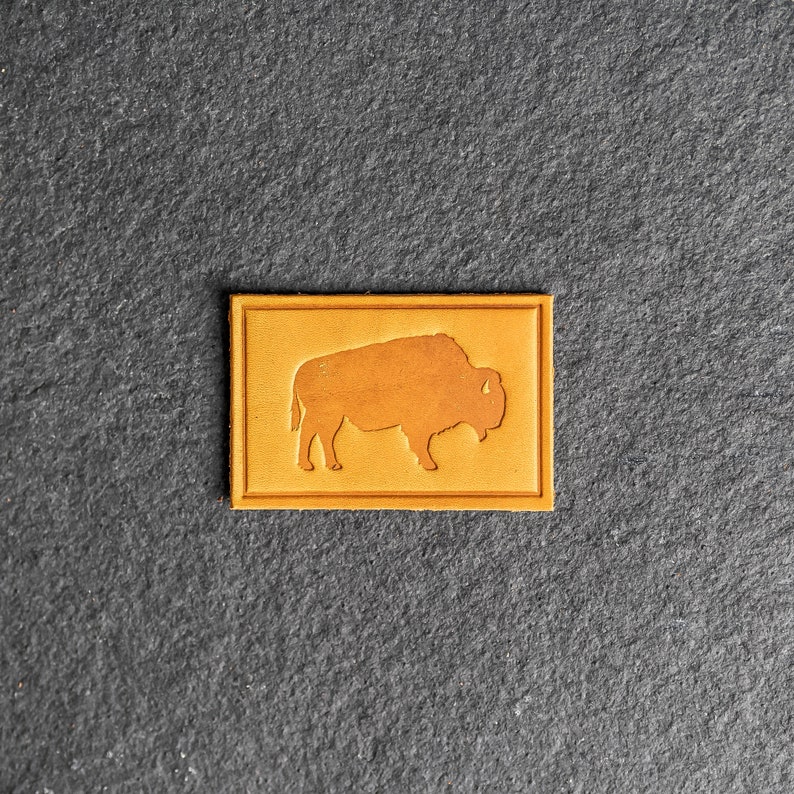 May include: A brown leather patch with a silhouette of a bison in the center.