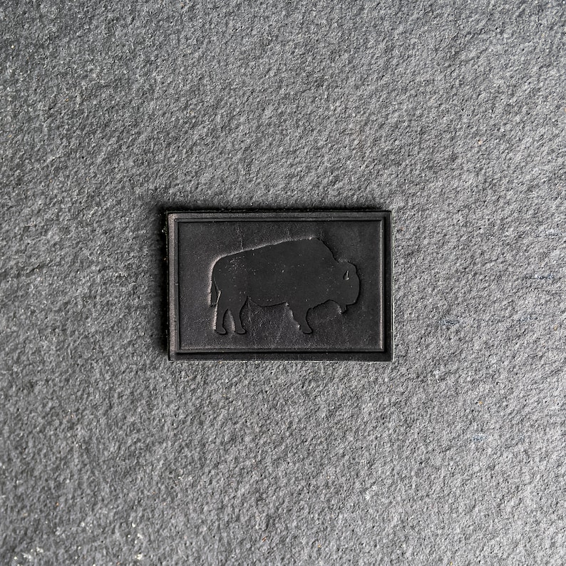 May include: A black leather patch with a silhouette of a buffalo in the center.