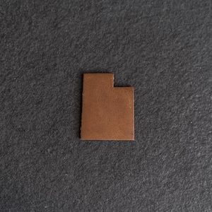 May include: A brown leather cutout of the state of Utah.