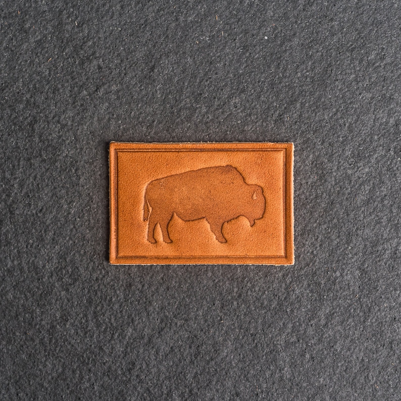 May include: A brown leather patch with a silhouette of a bison embossed in the center.