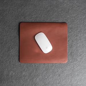 May include: A brown leather mouse pad with the initials "JWP" embossed in the bottom right corner. A white wireless mouse is on the pad.