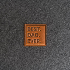 May include: A brown leather patch with the text "BEST. DAD. EVER." embossed in white.
