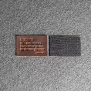 Peut inclure: Un patch en cuir marron avec la citation "L'éducation est l'arme la plus puissante que vous puissiez utiliser pour changer le monde." de Nelson Mandela. Le patch a une fermeture auto-agrippante noire au dos.