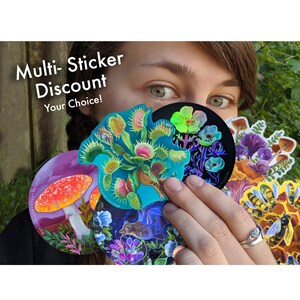 May include: A collection of colorful stickers featuring botanical and nature-themed designs, including a Venus flytrap, mushrooms, and bees. The stickers are held in front of a person's face, with the text "Multi-Sticker Discount Your Choice!" visible.
