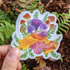 May include: A colorful sticker featuring a whimsical illustration of mushrooms, a snail, and foliage. The mushrooms have brown caps and purple stems, with a snail resting on a large orange and purple mushroom. The sticker has the text "marigoldartstudios.com".