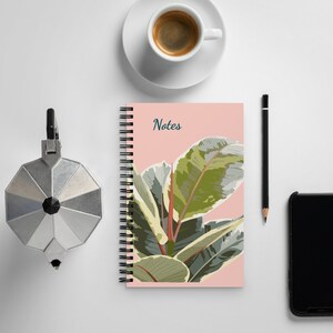 May include: A pink spiral bound notebook with the word "Notes" printed on the cover. The cover features a colorful illustration of a green and white leaf plant.