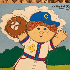 May include: A 9-piece jigsaw puzzle featuring a cartoon illustration of a child wearing a baseball uniform with the number 4 on the front. The child is throwing a baseball with a glove. The puzzle is titled "Let's Play Ball" and is from Golden Books.