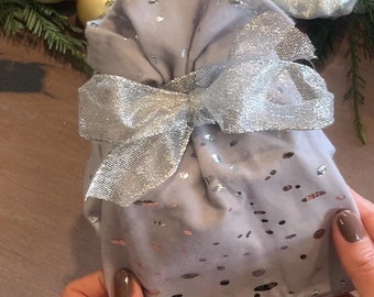May include: Two silver gift bags with silver glitter and white polka dots. One bag is tied with a white ribbon with silver stripes. The other bag is tied with a silver ribbon with a bow.