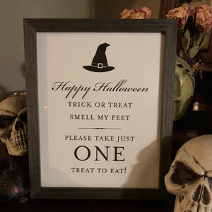 May include: A black and white sign with a witch's hat graphic and the text "Happy Halloween Trick or Treat Smell My Feet Please Take Just One Treat To Eat!"