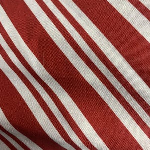 May include: A textile fabric featuring a repeating pattern of diagonal stripes in alternating shades of deep red and crisp white. The material displays a visible woven texture with consistent line widths running across the entire surface area.