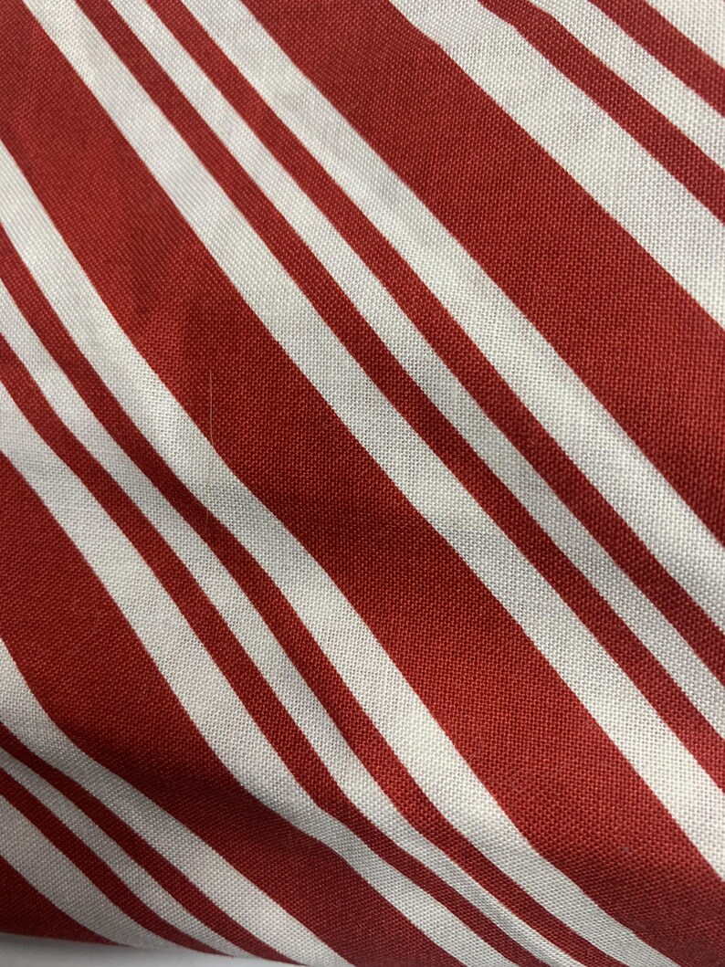 May include: A textile fabric featuring a repeating pattern of diagonal stripes in alternating shades of deep red and crisp white. The material displays a visible woven texture with consistent line widths running across the entire surface area.
