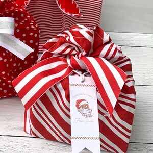 May include: A fabric gift wrap bundle featuring a red and white diagonal stripe pattern, tied with a matching striped ribbon. A white rectangular gift tag hangs from the ribbon, displaying a Santa Claus illustration and the text Special Delivery From Santa.