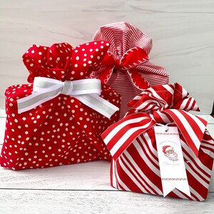 May include: Three fabric gift bags in red and white patterns. One bag features white polka dots and a white and silver ribbon. Another has red and white stripes. The third has red and white stripes and a tag reading Special Delivery From Santa.