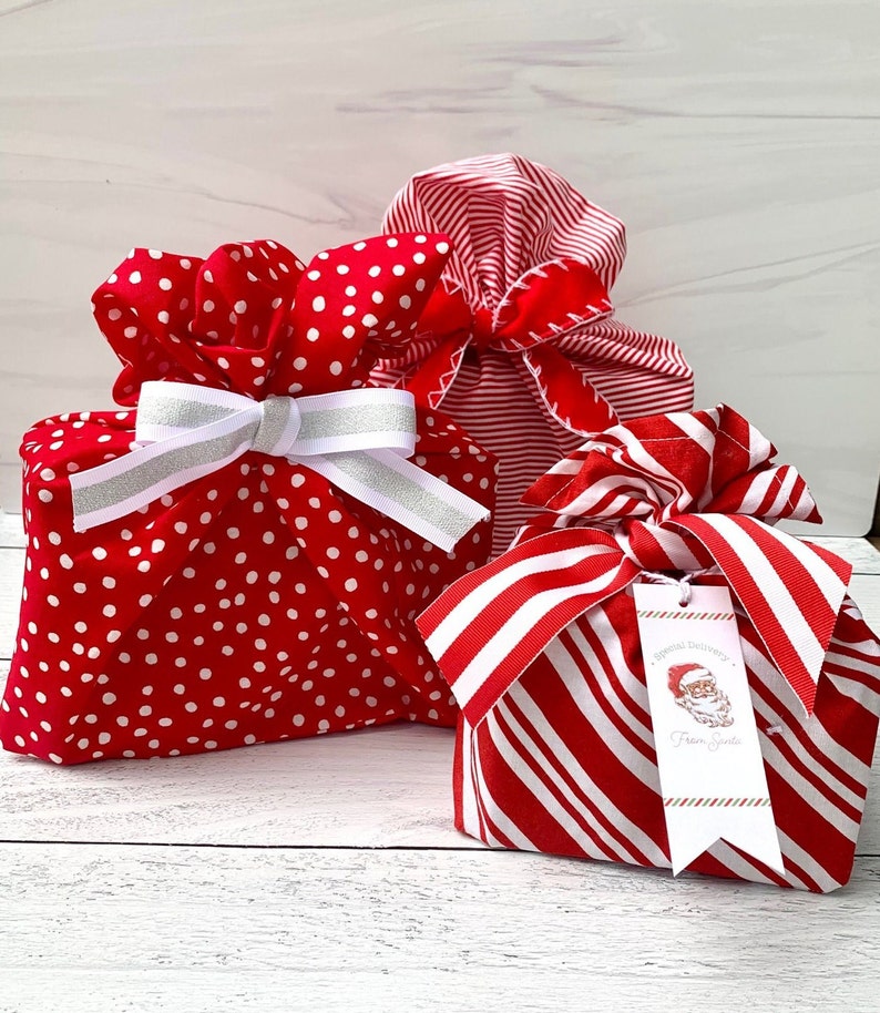 May include: Three fabric gift bags in red and white patterns. One bag features white polka dots and a white and silver ribbon. Another has red and white stripes. The third has red and white stripes and a tag reading Special Delivery From Santa.