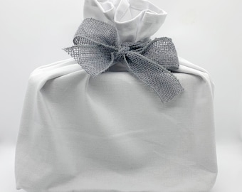 May include: A white fabric gift bag with a gray burlap bow. The bag is tied with a large bow and is ready for gift giving.
