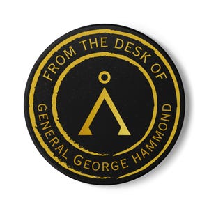 May include: A black and gold round sticker with the text "From the Desk of General George Hammond" and a gold symbol of a triangle with a circle on top.