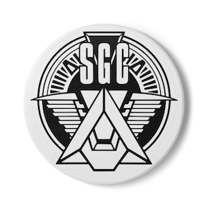 May include: Black and white circular logo with the text "SG-1" in the center. The logo features a stylized chevron with wings and a circle with radiating lines.