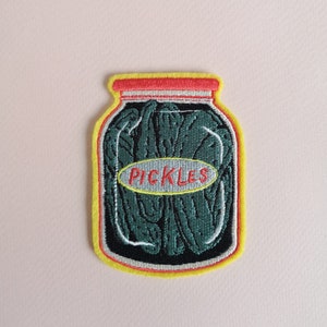 May include: An embroidered patch depicting a glass jar filled with green pickles. The jar has a white label with the word "PICKLES" in red letters.