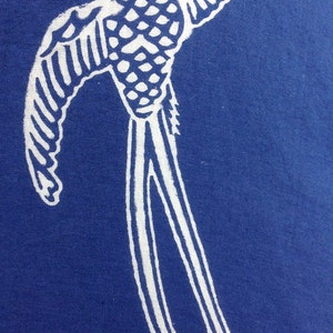 May include: White bird illustration on a blue background. The bird is depicted with outstretched wings and long, flowing tail feathers. The design has a vintage, hand-drawn aesthetic, with detailed patterns on the bird's body.