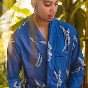 May include: A blue robe with a bird pattern. The robe has a shawl collar, a tie belt, and a pocket. The bird pattern is white and beige. The robe is made of a soft, flowing fabric.