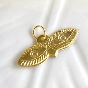 May include: Gold-toned pendant charm in the shape of a butterfly with two large eyes. The charm has a detailed, textured design.