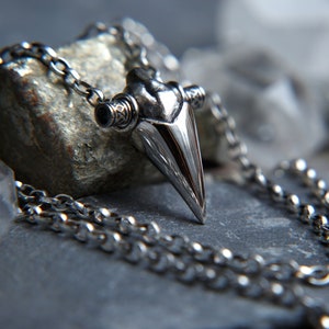 May include: A silver chain necklace with a sharp, pointed pendant that resembles a tooth. The pendant has intricate details and a polished finish.