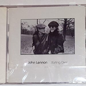 May include: A black and white photo of John Lennon and Yoko Ono on the cover of a CD. The text "John Lennon Starting Over" is printed below the photo.