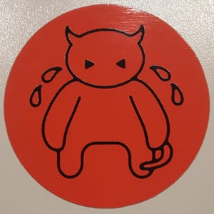 May include: A red circle sticker with a black outline of a cartoon devil with horns and a tail. The devil is crying black tears.